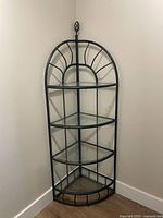 Full front view of metal corner shelf showing four glass tiers and arched metal frame