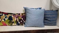 Group of cushions on bench: multicolour lumbar, denim blue square, blue-gold stripe square partially visible