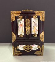 Front view showing doors with porcelain figure plaques, brass hardware, lower drawer