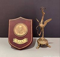 Front view of both items: brass stork statue and wooden plaque