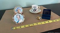 Overall lot showing two portrait plates on stands, cup with saucer, thimble, and presentation box with measuring tape for scale