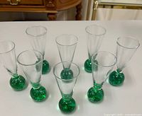 Front view of all eight clear glass shot glasses with green ball bases