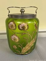 Front view showing green glass body, enamel floral motif, metal lid and handle