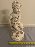 Front view of seated cherub holding puppy statue with tape measure for scale