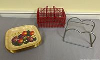 Stack of six fruit-design plates, red wire condiment caddy, silver wire napkin holder