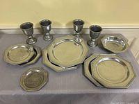 Front view of entire pewter-tone tableware set including goblets, plates, bowl