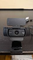 Front view of Logitech webcam showing lens, HD 1080p marking, privacy shutter, and clip mount