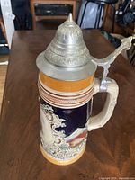 Overall view of ceramic beer stein showing pewter lid and relief design