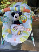 Full view of Bright Starts baby bouncer with toy bar and Mickey plush seated