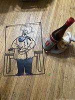 Metal wire chef wall hanging next to ceramic chef wine bottle holder with sample bottle