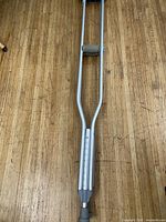 Full view of one crutch showing aluminum frame, foam pad, hand grip, and height scale.