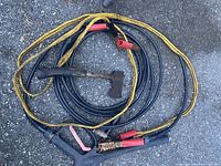 Hatchet, jumper cables, pressure washer hose, hacksaw arranged on ground