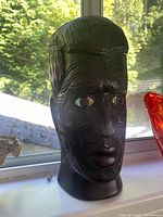Front view of carved Maori wooden head statue showing facial patterns and shell eyes