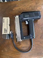 Overall view of HandyMaster electric nail⁄staple gun with attached power cord and box of Bostitch nails