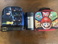 Front view of Batman lunch bag, Thermos jar, Super Mario lunch bag