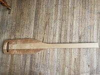 Full length view of paddle-shaped board on floor showing overall form and dimensions