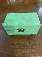 Closed green fabric-covered box with metal clasp