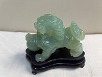 Full view of jade guardian lion on wooden stand, side angle