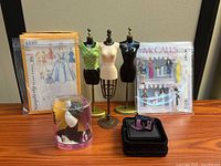 Group shot showing dress forms, both sewing patterns, Barbie accessory package, miniature handbag in velvet box