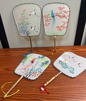 Front view of two fans upright showing bird and floral paintings