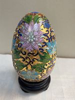 Front view of cloisonné enamel egg on stand showing floral design and gold background
