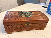 Full view of carved wooden jewelry box with latch and feet