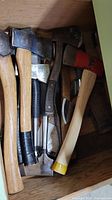 Drawer of assorted axes and hatchets showing heads and handles