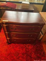 Front view of dark wood dresser with three doors, curved front, brass-tone pulls