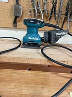 Makita BO4557 palm sander left side showing dust bag, cord and pad