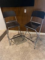 Two black folding bar chairs standing side by side