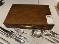 Closed wooden chest with loose serving pieces and knives displayed in front