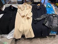 All four coats laid out: black, cream, navy long coats and black leather jacket