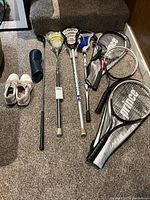 Group shot of three tennis racquets, three lacrosse sticks, one golf club, pair of golf shoes and headcover