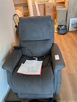 Front view of dark grey VivaLift power lift recliner with remote and manuals on seat
