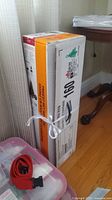 Boxed 4ft pre-lit tree standing upright beside table, part of pink storage bin visible