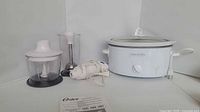 Group shot showing Crock-Pot slow cooker with lid, Oster hand blender components and manual
