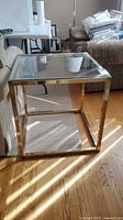Full view of square glass top end table with brass-tone frame