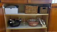 Cabinet shelf holding Pyrex bowls, glass juicer, mandoline, baskets, additional kitchen items