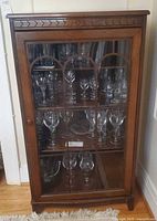 Front view of wood glass-front cabinet with arched muntin glass door and interior shelves