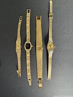 Five gold-tone women’s wristwatches laid flat side by side on dark background