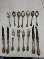 Full set of 14 sterling flatware pieces laid out: 6 spoons, 4 forks, 4 knives