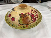 Top view of tagine lid showing painted chicken, red accents, green rim