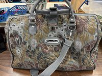 Front view of floral tapestry duffle with handles, shoulder strap and logo plaque