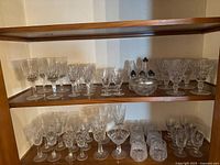 Three shelf view showing variety of clear cut crystal stemware, tumblers, dessert bowls and five miniature salt shakers