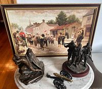 Overall lot showing framed print, two sculptures and tabletop cannon on marble table