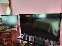 Hisense TV on glass stand with remote and Sceptre monitor on dresser