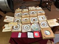 Overview of approximately 18 boxed collector plates displayed on table
