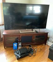Front view of Sony 65-inch TV on wood stand with DVD player and cables visible