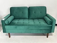 Front view of green velvet loveseat with bolster pillows and tufted cushions