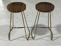 Front view of both bar stools showing wood seats and gold-tone metal legs